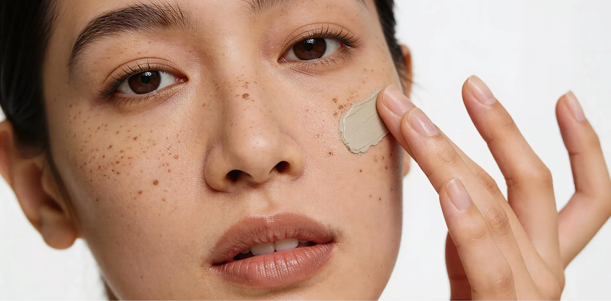 Mujer con pecas aplicándose crema hidratante en la mejilla.